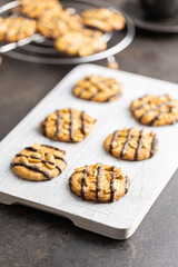 Chip cookies with peanuts and chocolate strips on white cutting board.