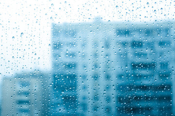 Window covered with water drops with houses in the background, rain in the city