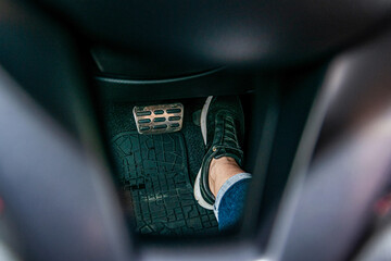 Close-up foot in sports shoes presses on the pedal in the car