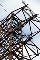 A fragment of a high-voltage transmission line support against the sky. Rusty metal among clouds in a blue sky