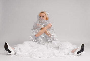 happy funny bride sitting in wedding dress and veil on white background