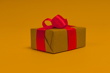gift wrapped in paper with a red ribbon on a yellow background, close-up