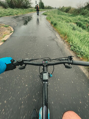 Fototapeta na wymiar POV of cycling during heavy rain. A man holds handlebar with one hand during pouring rainfall