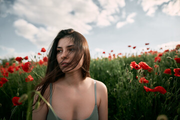 Naklejka premium Beautiful young girl in the red poppy field. Brunette woman with naked shoulders outdoors. Concept of women's relaxation and happiness in the rural nature