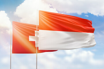 Sunny blue sky and flags of indonesia and switzerland