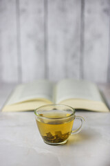 Brewed herbal green tea in a transparent cup in front of an open book on a light background.