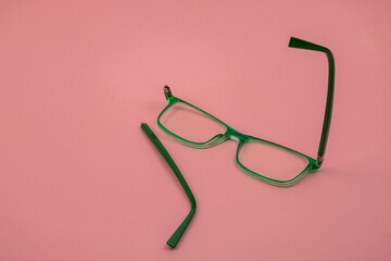 Green glasses with a broken temple against a pink background.