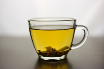 Brewed herbal green tea in a transparent cup on a dark table with a bright white light on the background