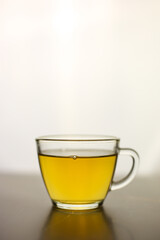 Brewed herbal green tea in a transparent cup on a dark table with a bright white light on the background