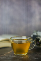 Brewed herbal green tea in transparent cup near open book and vintage camera on dark background