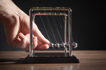 Male hand showing Newton's cradle balls on the wooden table. Business