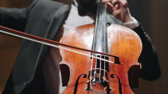 violoncellist is playing cello in philharmonic hall, concert of classical music, closeup view on hands with bow