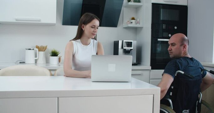 man in wheelchair and his wife using laptop at home. Help. High quality 4k footage