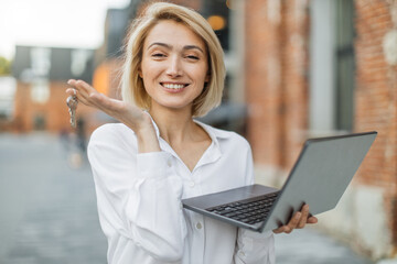 Real estate attractive agent beautiful woman with house keys and laptop in front of sold apartment,...