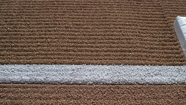 A slider shot along a freshly groomed first base path and white baseline as a baseball rolls up stopping at first base