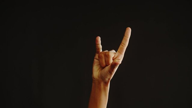African American man showing rock and roll gesture with fingers isolated on black background. Guy holding hand up close-up.