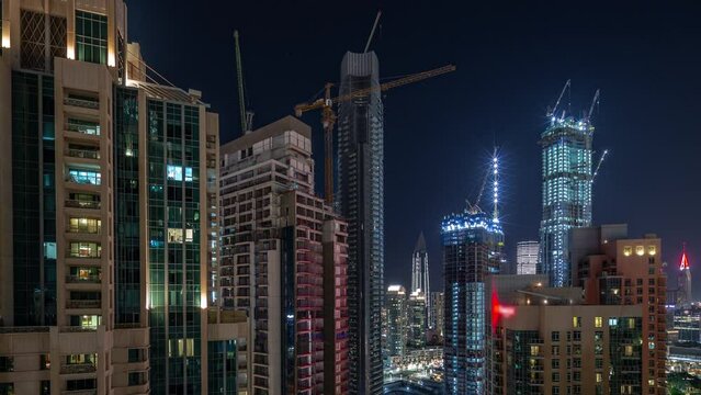 Cranes working on big constraction site works of new skyscrapers night timelapse. Urban skyline of high-rise towers and building activity in Dubai downtown