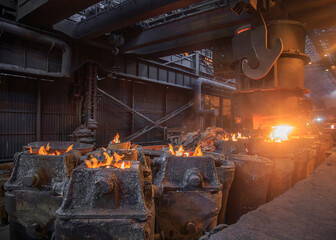 Steel pouring from casting ladle into metal molds.