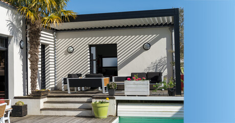 Trendy outdoor patio pergola shade structure, awning and patio roof, garden lounge, chairs, metal grill surrounded by landscaping