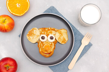 Funny monkey,dog face shape snack from pancake,cheese on plate. Cute kids childrens baby's sweet dessert, healthy breakfast,lunch, food art with milk,apples on gray concrete background,top view