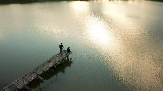 The guys on the old wooden bridge on the lake, fishing at sunset, summer landscape in the village, rest on the lake in summer
