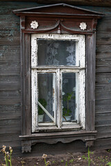 Obraz na płótnie Canvas Brown carved platband cracked glass window of old traditional russian wooden house