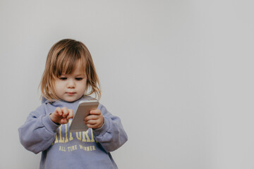 Little girl in violet hoodie using a phone on white background