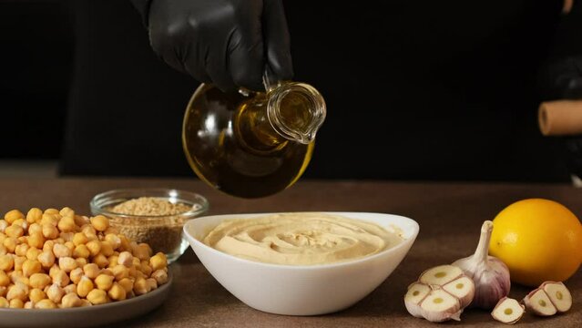 Pouring olive oil in Chickpea hummus made from mashed chickpeas dip with tahini lemon garlic close-up. Enjoying yummy hummus with pita, lavash, bread sticks, grissini. Kosher healthy vegan food. Lean 