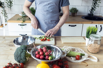 Handsome father, strong young man cooking healthy vegetable salad with fresh organic ingredients, tasty food in the kitchen at home . Men doing chores. Ripe pepper, tomato, cucumber