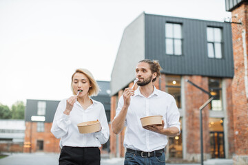 Caucasian businessman and businesswoman eating healthy salad during lunch time at work. Concept of healthy food rest and break. Attractive business people walking on city street.