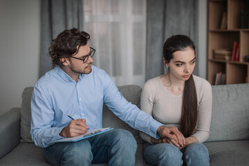 Serious european handsome young male psychologist in glasses calming sad woman patient in clinic