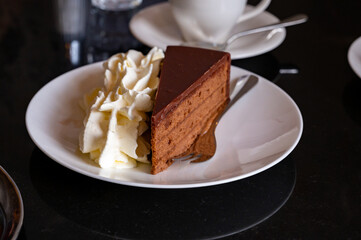 Piece of famous Sachertorte chocolate cake with apricot jam of Austrian origin served with whipped cream