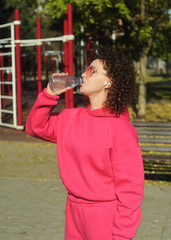woman with a headphones drinking water on the playground 