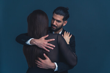 Seductive good-looking elegant guy looking affectionately at his young brunette wife, holding her tight. Studio shot. High quality photo