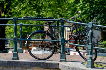 Vintage classic bicycle parked along the canal bridge of Amsterdam with blurred traditional houses as background, Cycling is a common mode of transport in Holland, Netherlands land of bicycle.