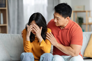 Loving asian man consoling his crying wife, home interior