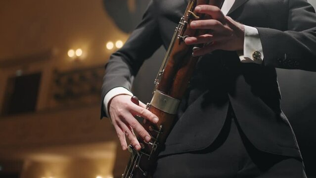musician with bassoon on scene of opera house or philharmonic hall, closeup of hands