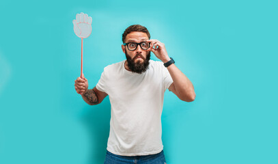 Young caucasian charismatic man holding a fly swatter wanting to kill annoying mosquito or a fly.