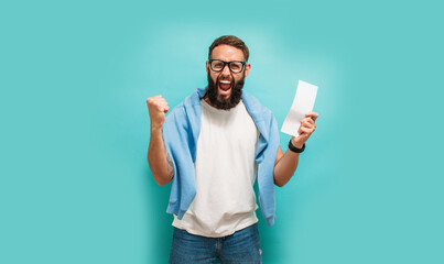 Excited happy young male winner feeling joy winning lottery, placing bets, getting cashback online gift isolated on blue background. Human face emotions and betting concept. Trendy colors - obrazy, fototapety, plakaty