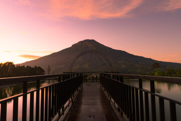 Mount Sumbing with sunrise sky and bridge on the foreground. There is artificial lake surrounded the bridge. Embung Kledung, Central Java, Indonesia