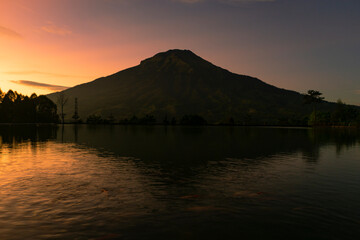 Sunrise with Mount Sumbing with lake surface on the foreground. The lake surface make reflection of mountain and sunrise sky. Embung Kledung, Central Java, Indonesia
