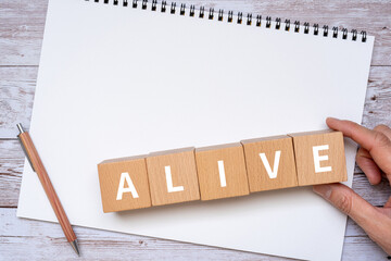 「ALIVE」と書かれたブロック、ノート、ペン、手