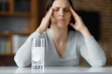 Upset young woman suffering from headache using soluble drug for pain relief. Exhausted woman...