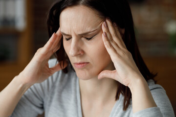Upset young woman suffering from headache. Exhausted woman with closed eyes massaging the temples...