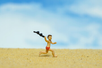 Miniature people toy figure photography. A child having fun running on the beach. Beautiful bright beach landscape background