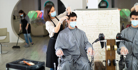 Man client in mask during hair cut by professional hairdresser in mask at beauty salon