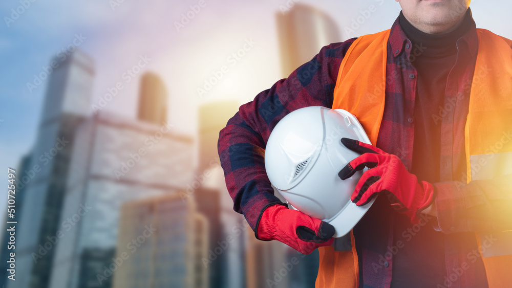 Poster man with construction helmet in his hands. man with white helmet. builder in front of downtown. buil