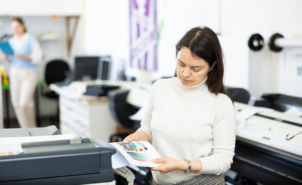 Female employee of the copy center checks the quality of the print on the color chart