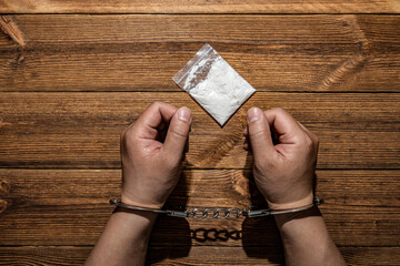 man locked by handcuffs with pack of white powder in front - obrazy, fototapety, plakaty