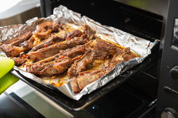 lady taking out a fresh baked home-made pork ribs from an oven
